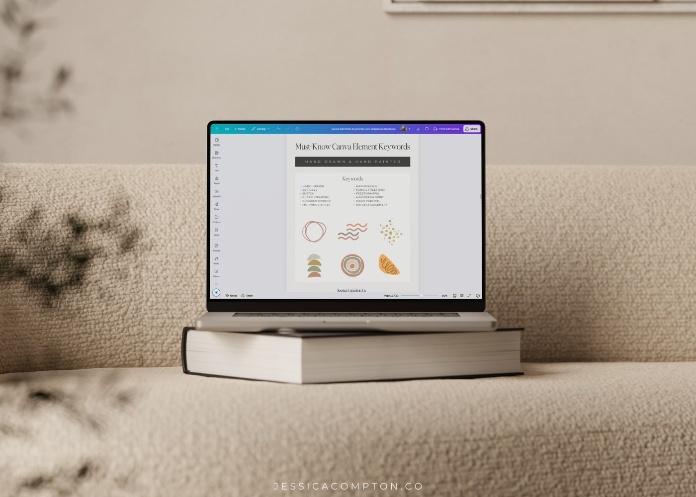 Open laptop showing Must-Know Canva Element Keywords freebie, sitting on top of book on tan colored couch